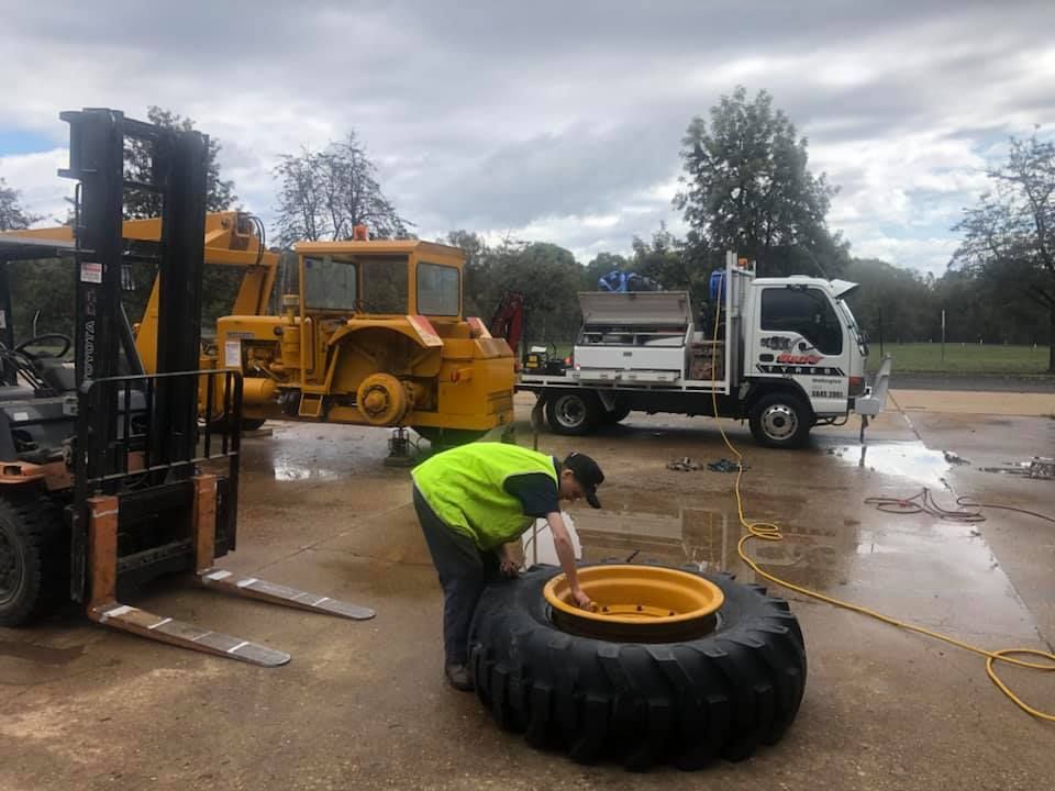 Person working on large tire near construction vehicles, outdoors. — Ben's Tyres in Wellington, NSW
