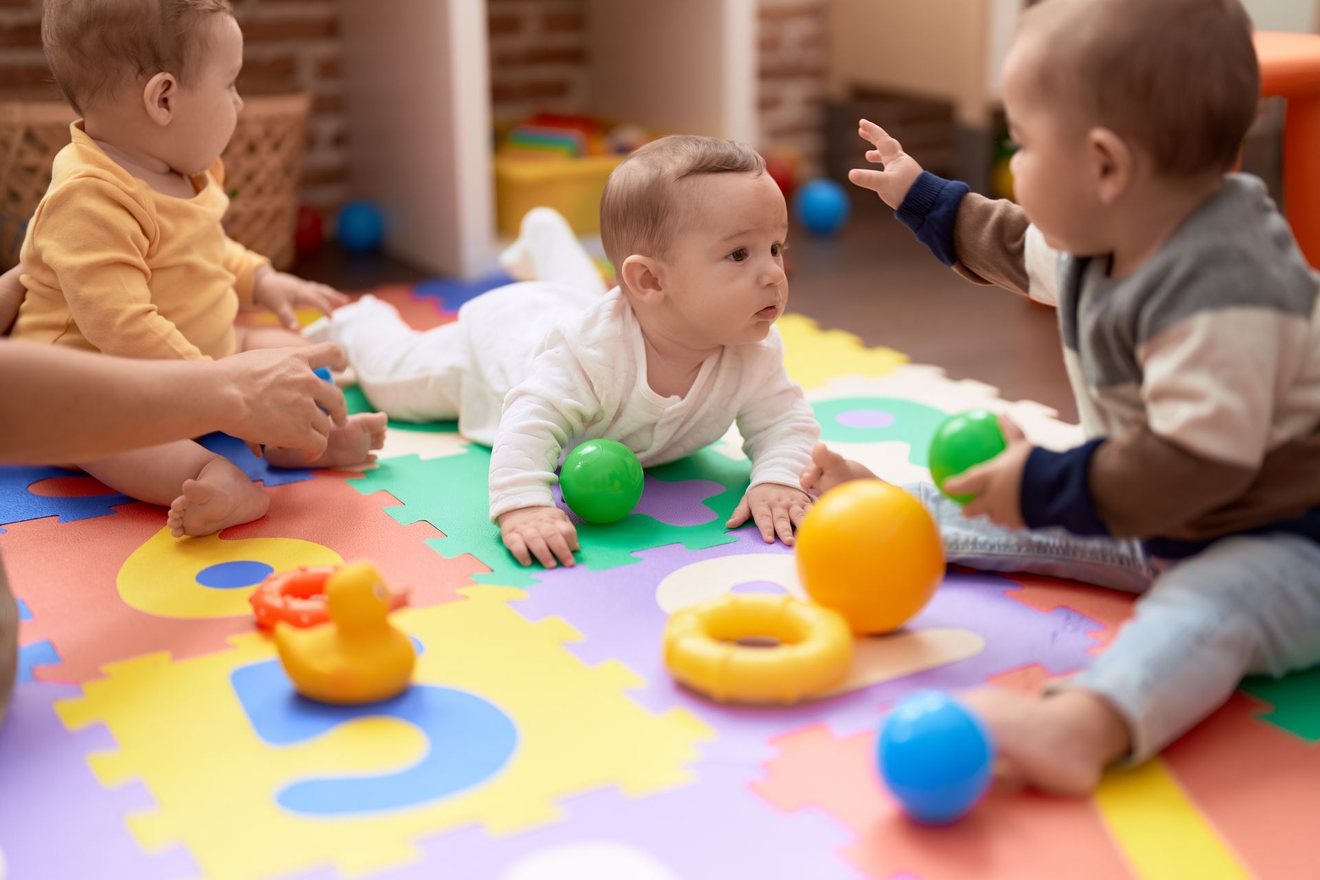 Three babies are playing with toys on a puzzle mat.