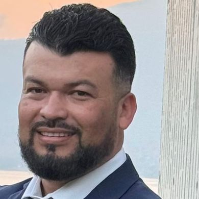 A man with a beard is wearing a suit and tie and smiling.