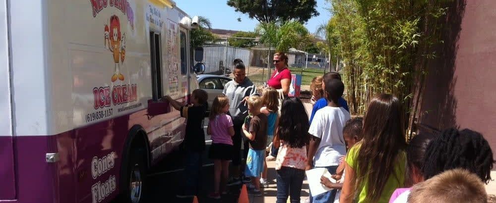 People lining up beside a pink-and-white truck at a sunny outdoor event