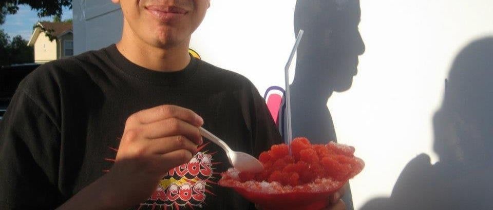Person eating red watermelon from a bowl in bright sunlight, with shadows on the wall behind.
