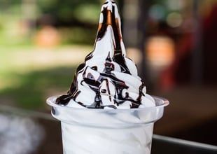 White soft-serve ice cream topped with chocolate syrup in a clear cup