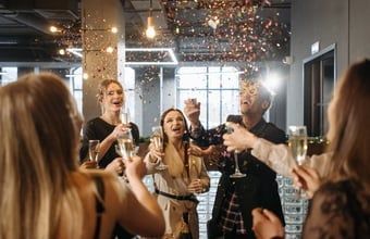 People celebrating indoors with confetti and drinks, smiling and raising glasses at a party