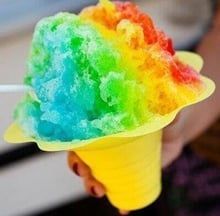 Rainbow shaved ice in a yellow cone cup, held in hand.