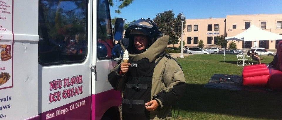 Person in protective gear beside an ice cream truck at an outdoor event.