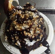 Chocolate dessert topped with whipped cream and crumbs, drizzled with dark sauce on a white plate