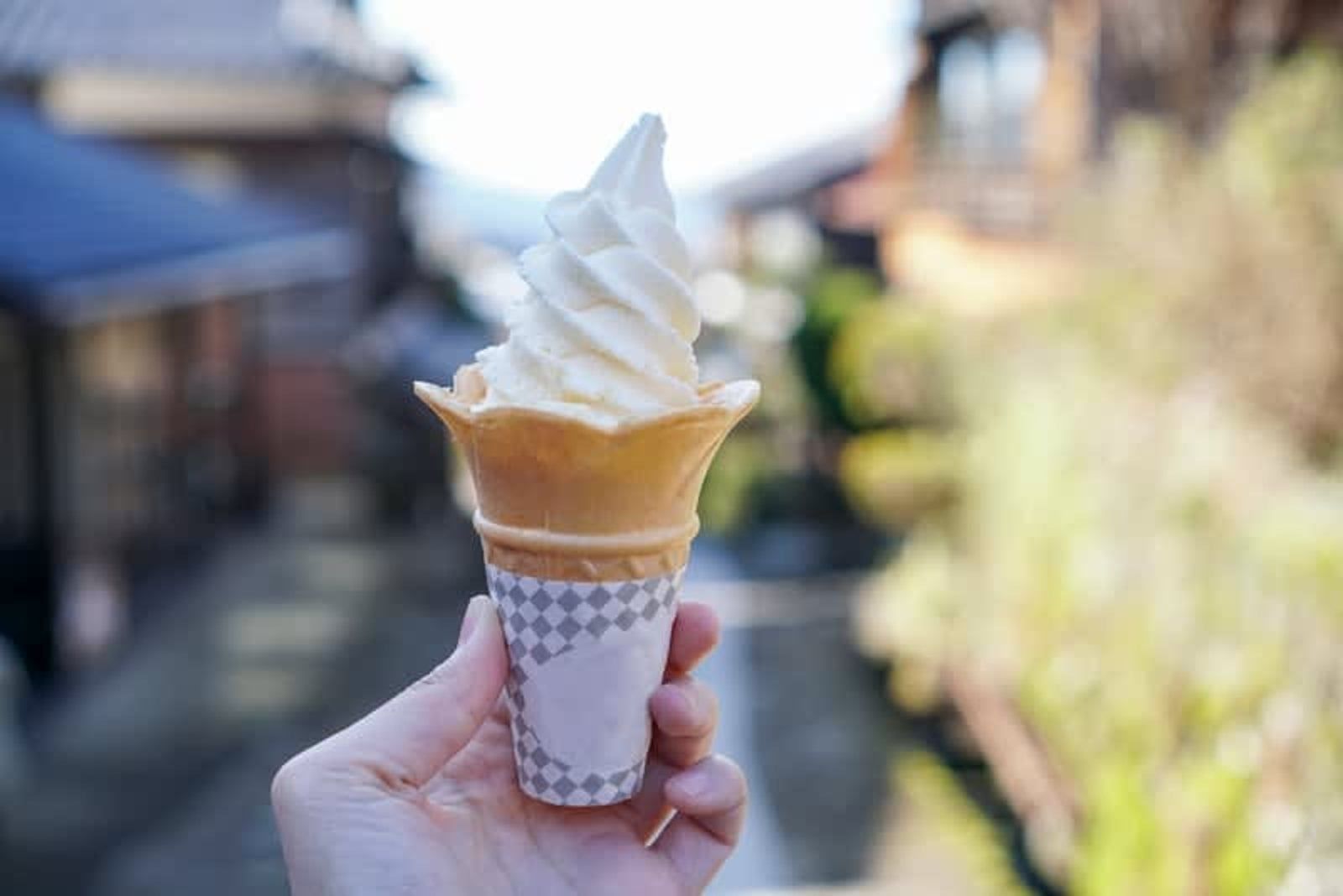 Hand holding a soft-serve ice cream cone outdoors with a blurred street background