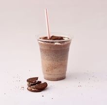 Iced coffee in a clear cup with a straw, topped with crumbs, beside two cookies on a white background