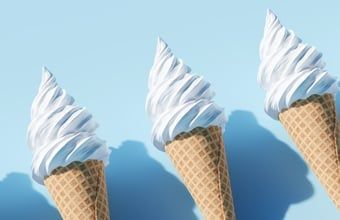 Three vanilla soft-serve ice cream cones against a light blue background.