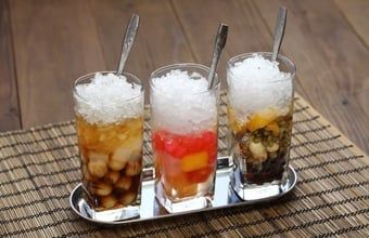 Three layered iced drinks with crushed ice and straws on a tray over a woven mat.