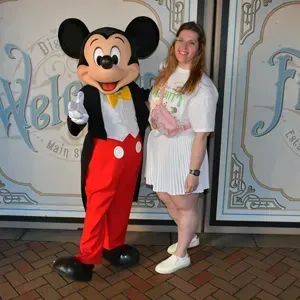 Woman posing with Mickey Mouse in front of a decorative wall, both smiling.