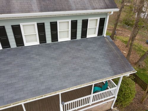 Aerial view of a house with gray shingle roof, black shutters, and a covered front porch.