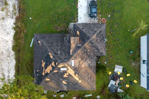 Aerial view of a house roof with a parked car, lawn, and scattered debris on the right side.