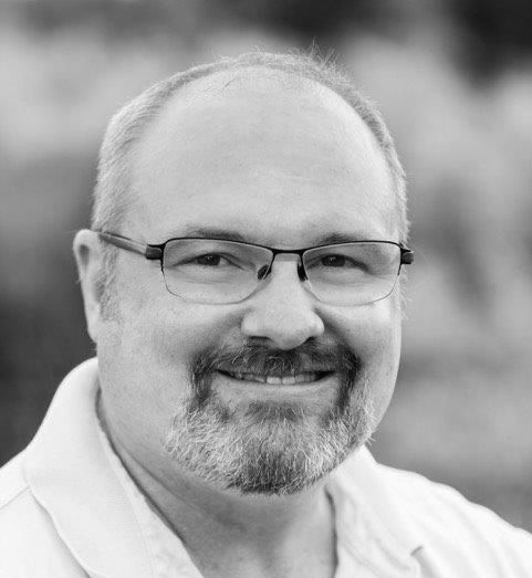 Smiling man with glasses and goatee in a black-and-white portrait.