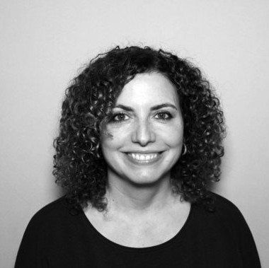 Portrait of a smiling person with curly dark hair against a plain light background