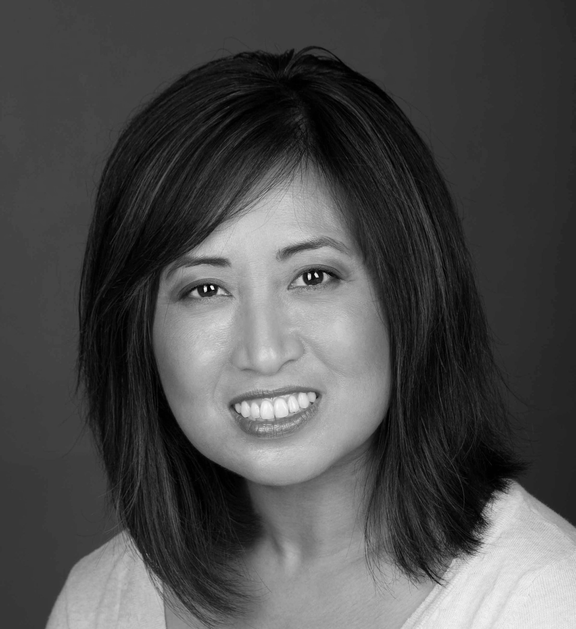 Black-and-white portrait of a smiling person with shoulder-length hair against a plain background