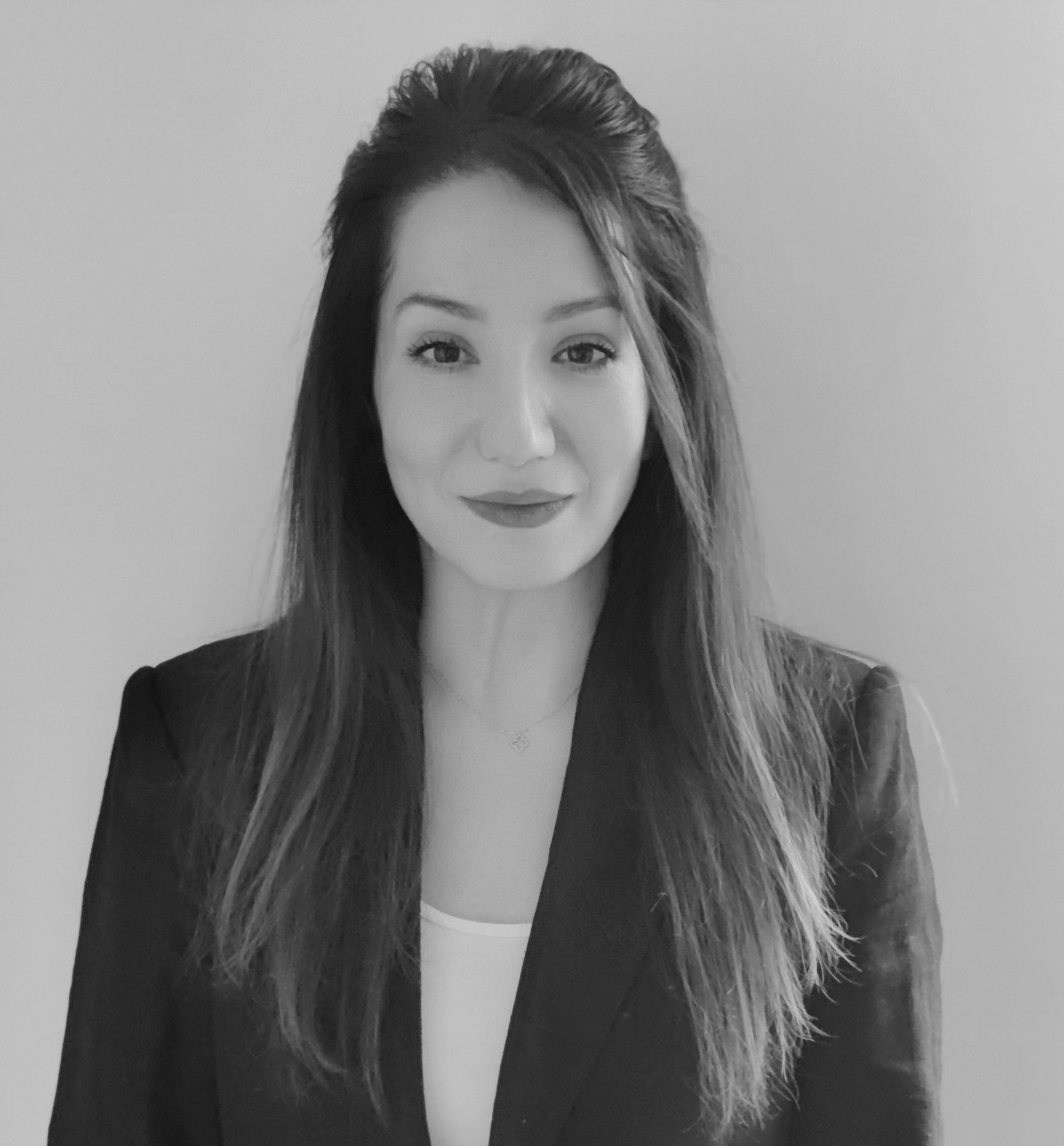 Black-and-white portrait of a woman with long hair wearing a blazer, facing the camera and smiling gently