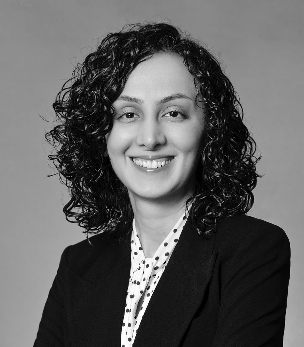 Smiling person in a black blazer over a white patterned blouse on a gray background