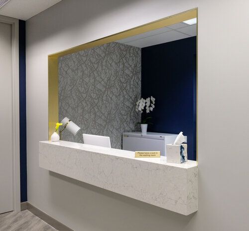 Modern reception desk with a gold-framed mirror, gray textured wall, and dark blue accent wall.