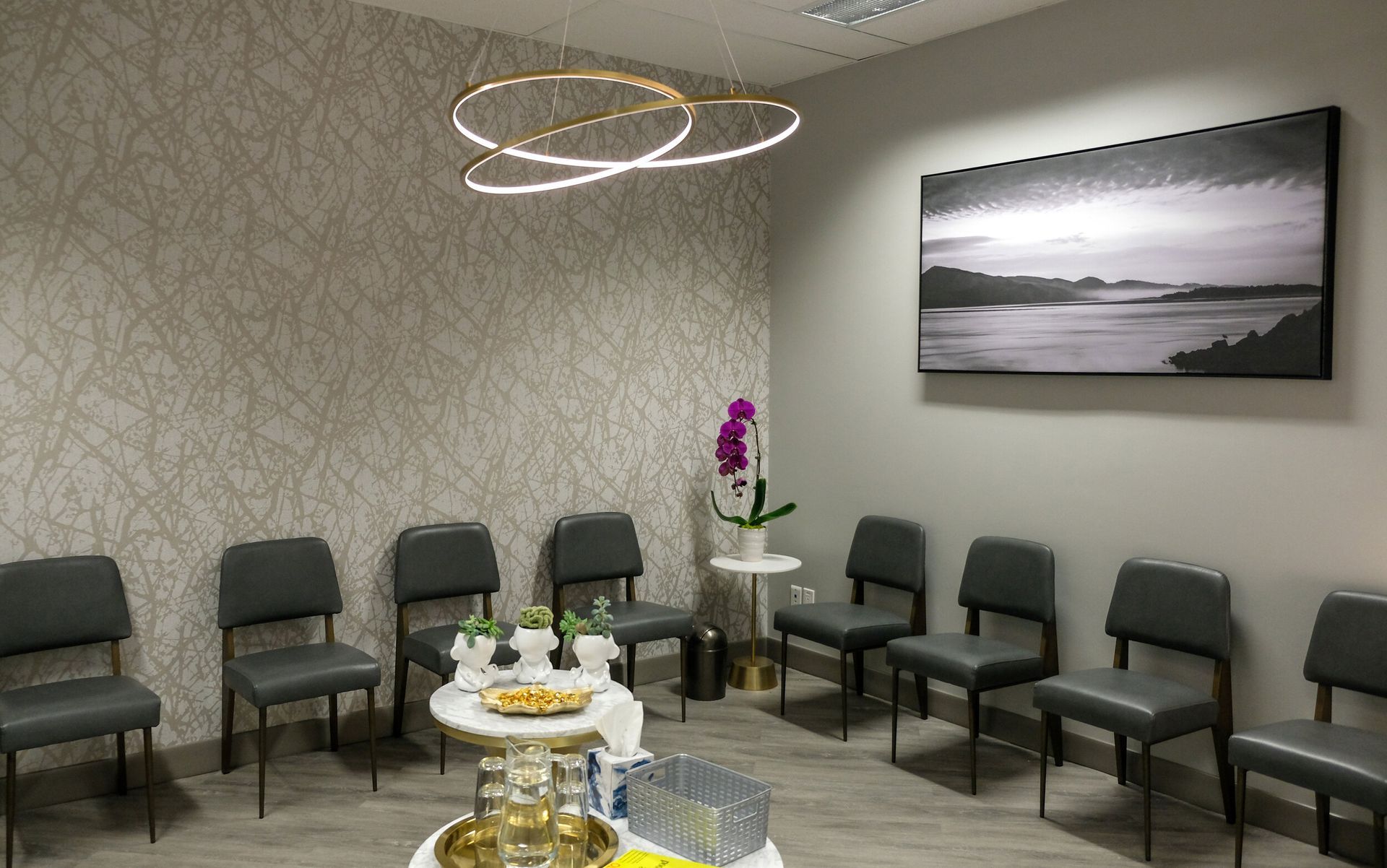 Modern waiting room with gray chairs, glass tables, orchid, and black-and-white wall art