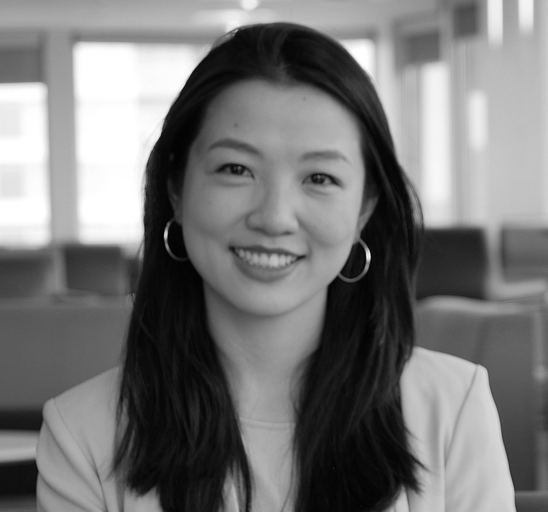Smiling woman with long dark hair in a blazer, seated in a bright office setting