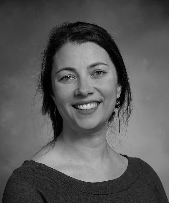 Smiling woman in a dark top, posed against a gray studio backdrop.
