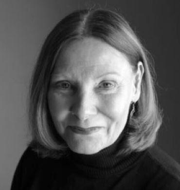 Black-and-white portrait of a person with shoulder-length hair and a slight smile, wearing a dark turtleneck.
