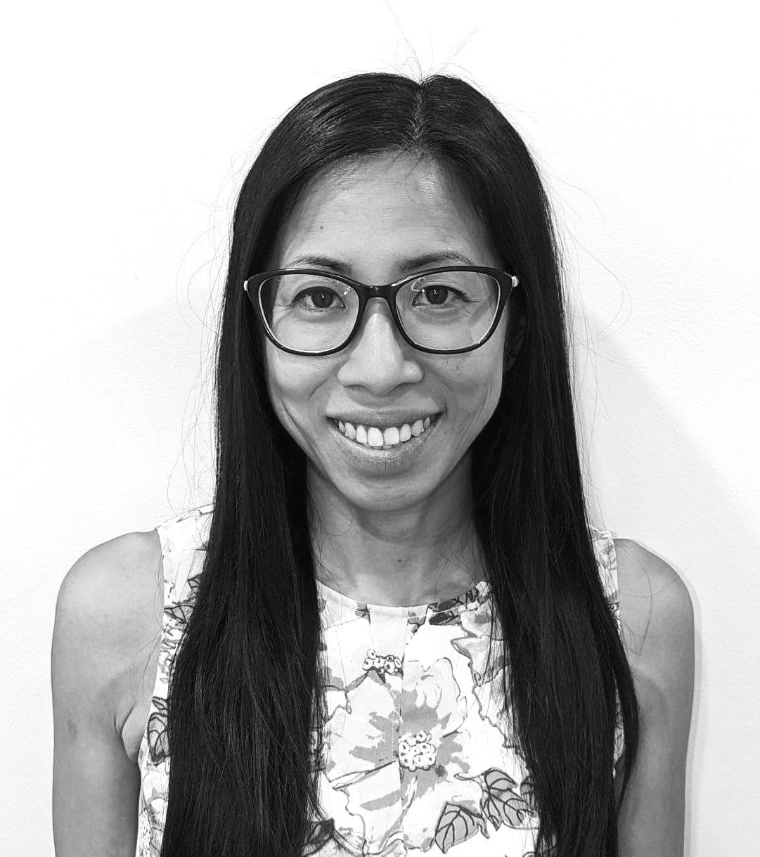 Smiling person with long dark hair and glasses, wearing a floral top against a plain background
