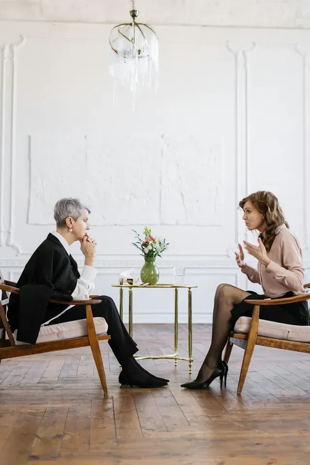 Two people in conversation seated across a small table in a bright, minimalist room