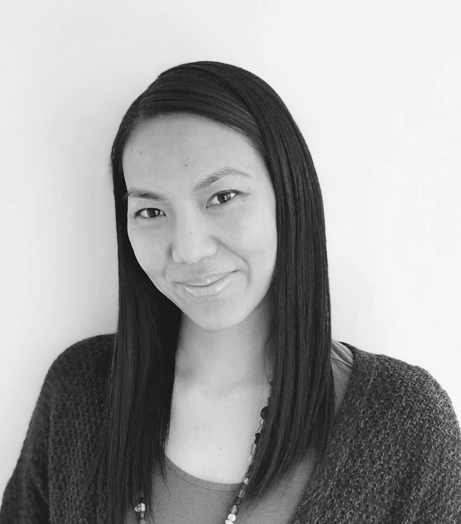 Portrait of a person with long straight hair, smiling slightly against a plain background