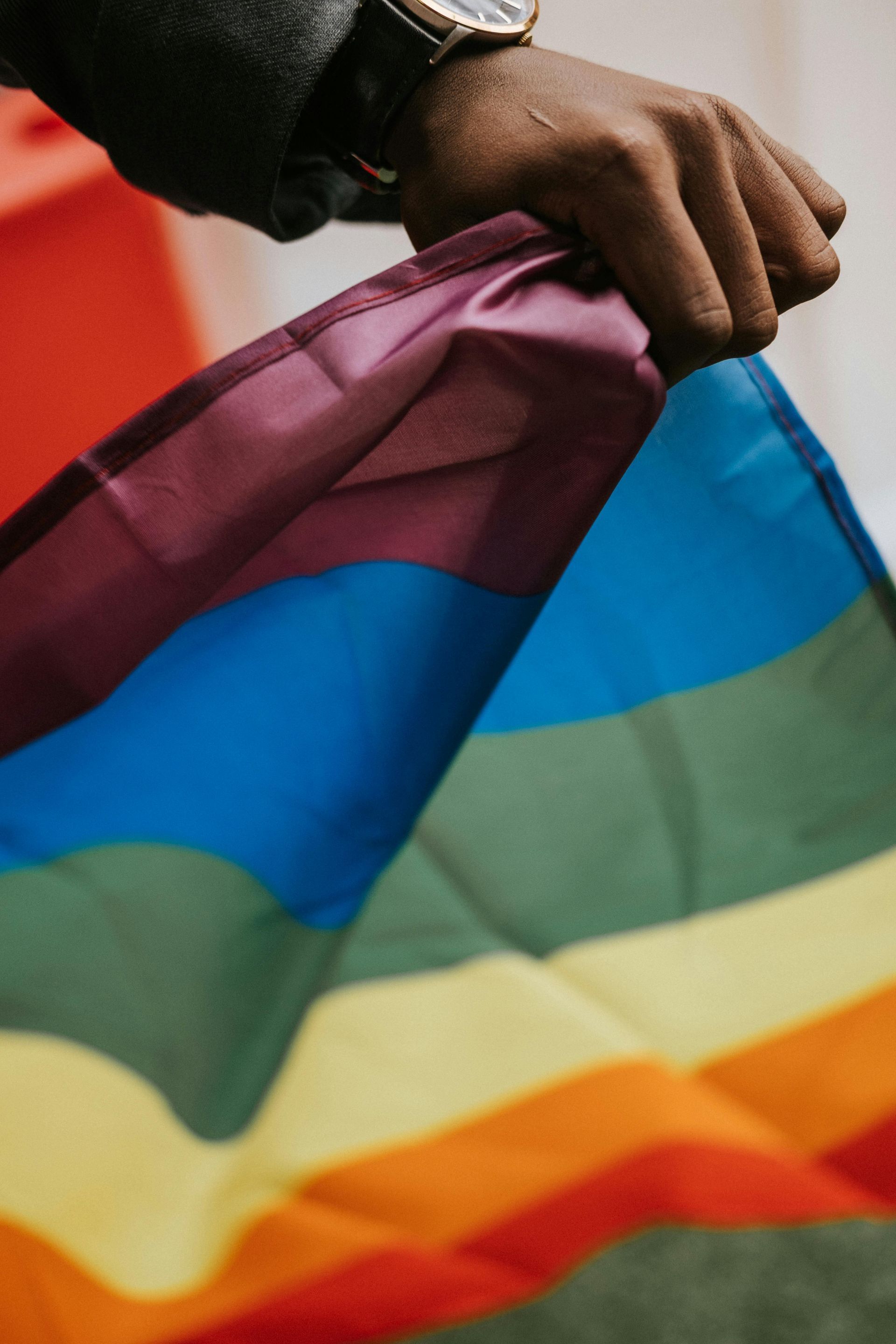 Hand holding a rainbow Pride flag with colorful stripes fluttering in the wind
