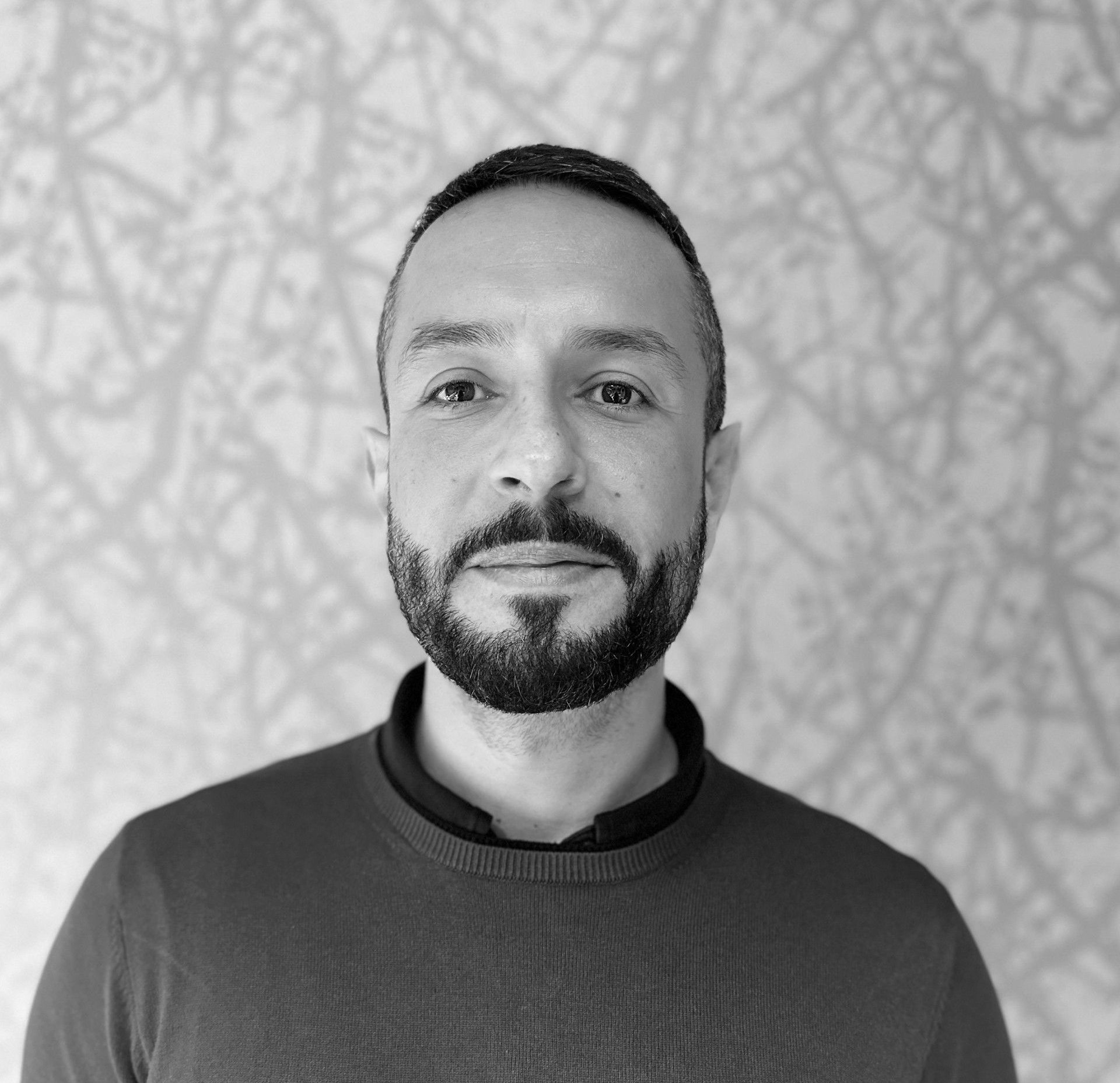 Portrait of a man with a beard in a dark sweater against a textured gray background