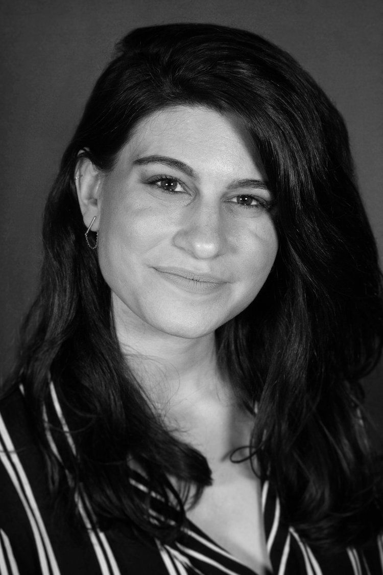 Black-and-white portrait of a person with long dark hair, smiling slightly against a plain background