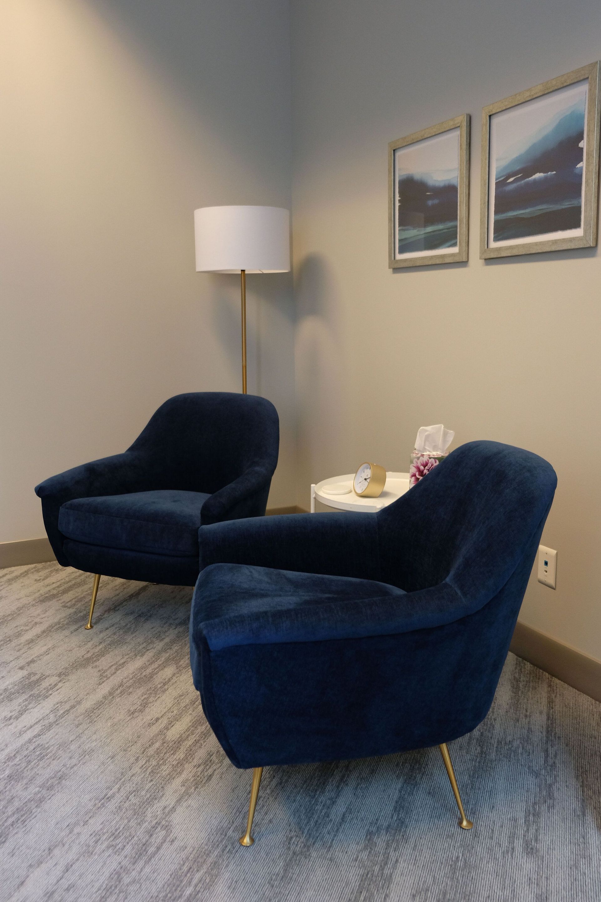 Two navy chairs in a quiet corner with a floor lamp, small table, and framed wall art.