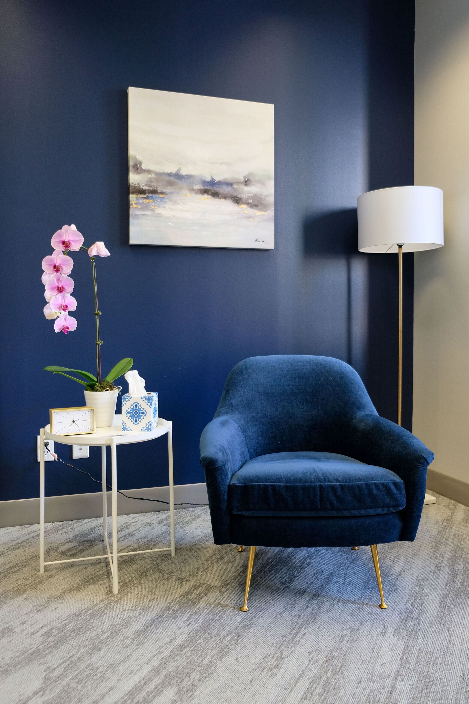 Blue accent chair beside a white floor lamp and side table with pink orchids in a modern room