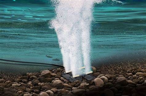 Underwater view of a white fountain jet rising from a rocky seabed into blue-green water
