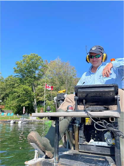 Person in a motorized wheelchair near water with a small Canadian flag and blue sky in the background