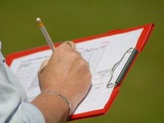 Hand holding a pencil over a red clipboard with papers outdoors