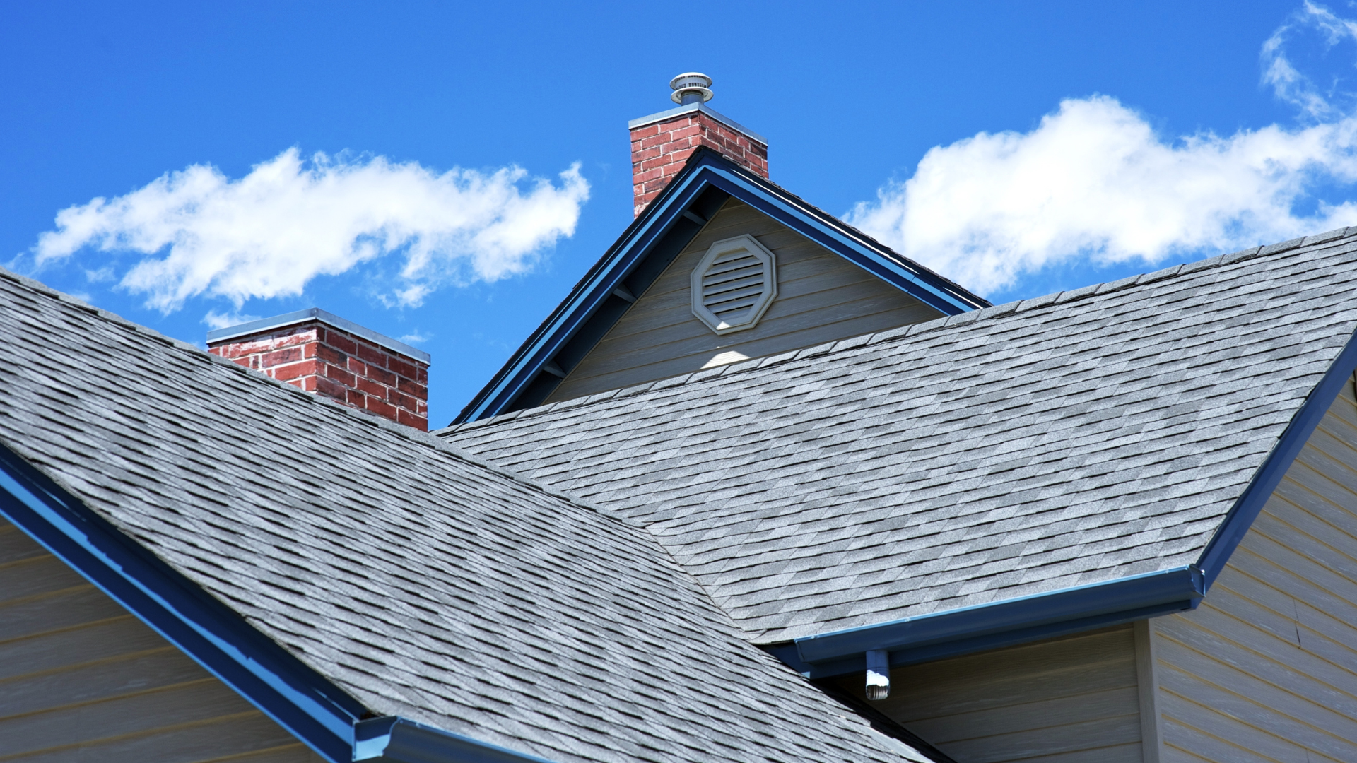 Gray shingle roofs against a blue sky with white clouds. Red brick chimneys visible.