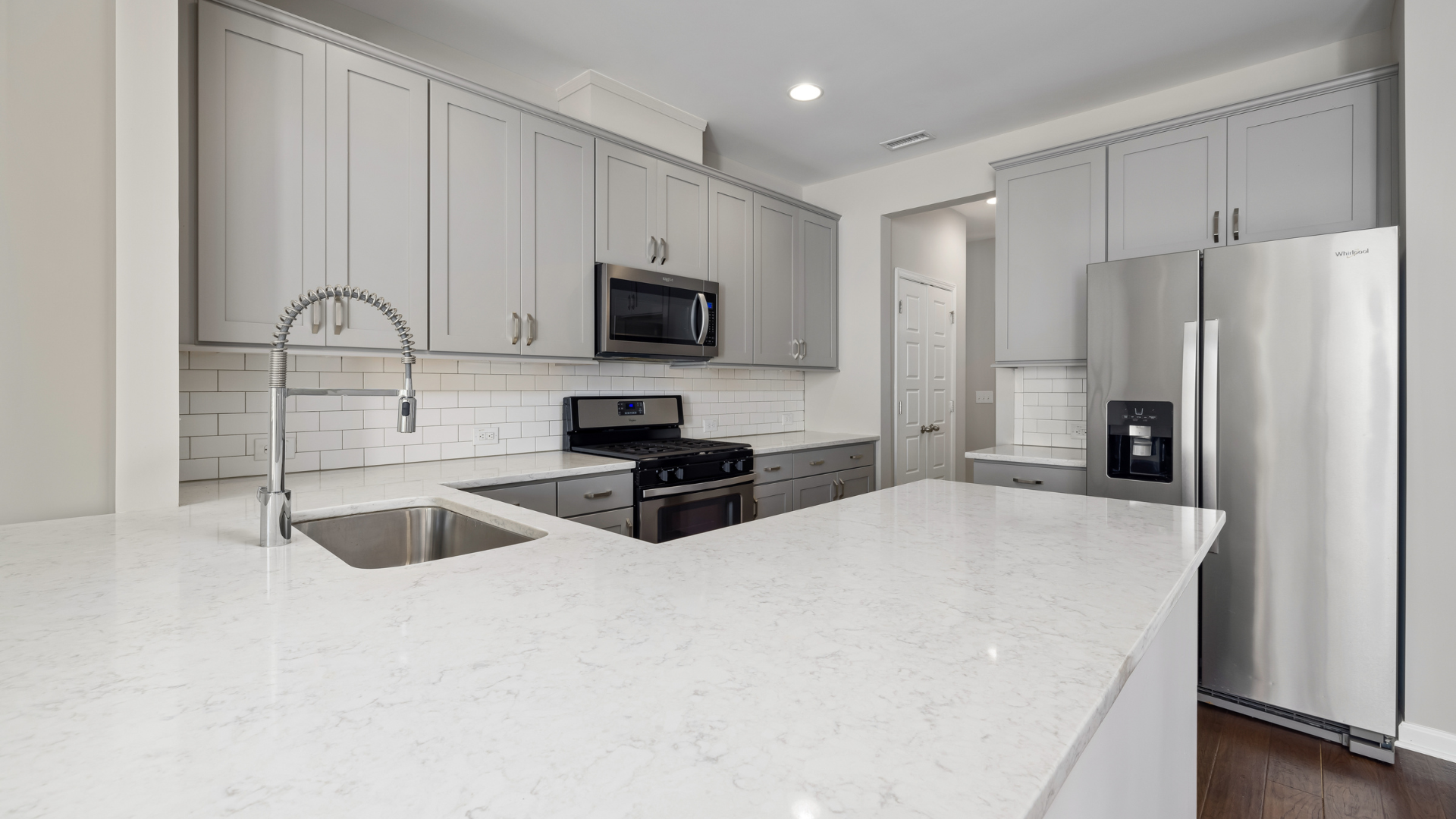 Modern kitchen with gray cabinets, stainless steel appliances, and white countertops.