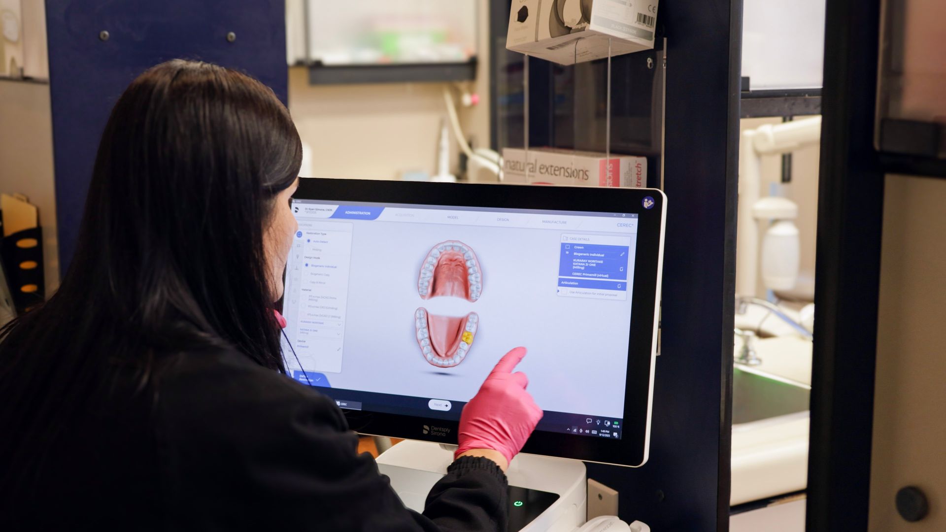 Person in pink gloves points at dental scan on a computer screen in a dental office.