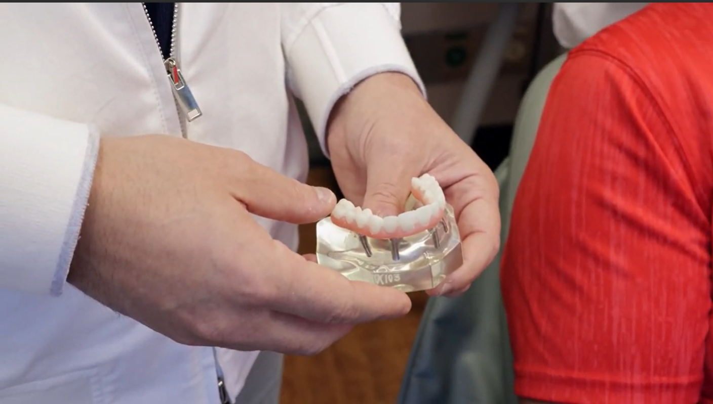Person in white coat holds dental model with dentures.