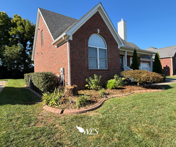 Brick house with green lawn and flower bed under a clear, blue sky.