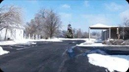 A snow-covered street and surroundings on a sunny day. Buildings and trees are dusted with white, with a clear blue sky above.
