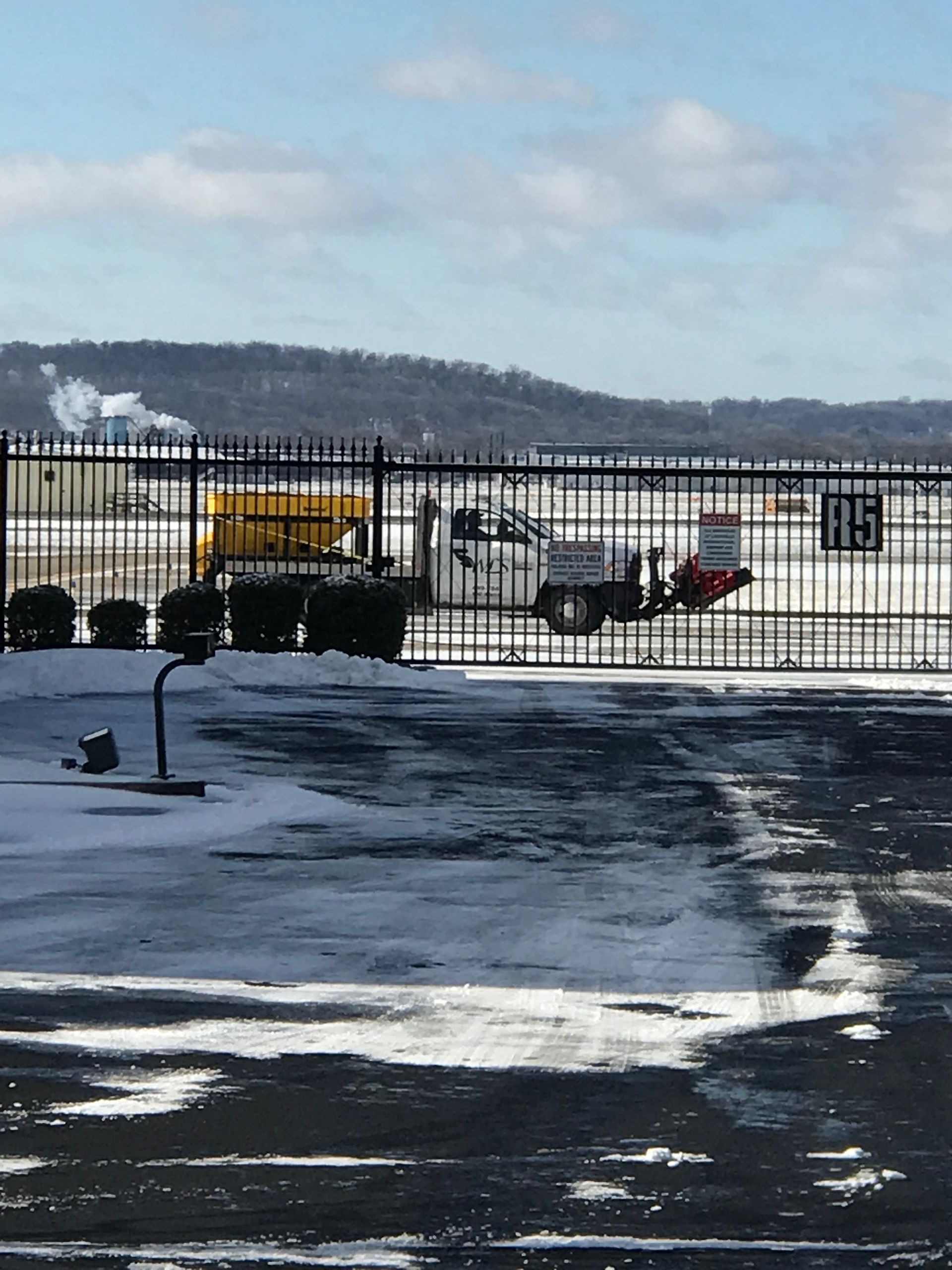 Snowy tarmac with a small airplane near a fence, with hills in the background.