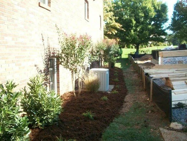 A landscaping project next to a brick building features mulch, young plants, and lumber.