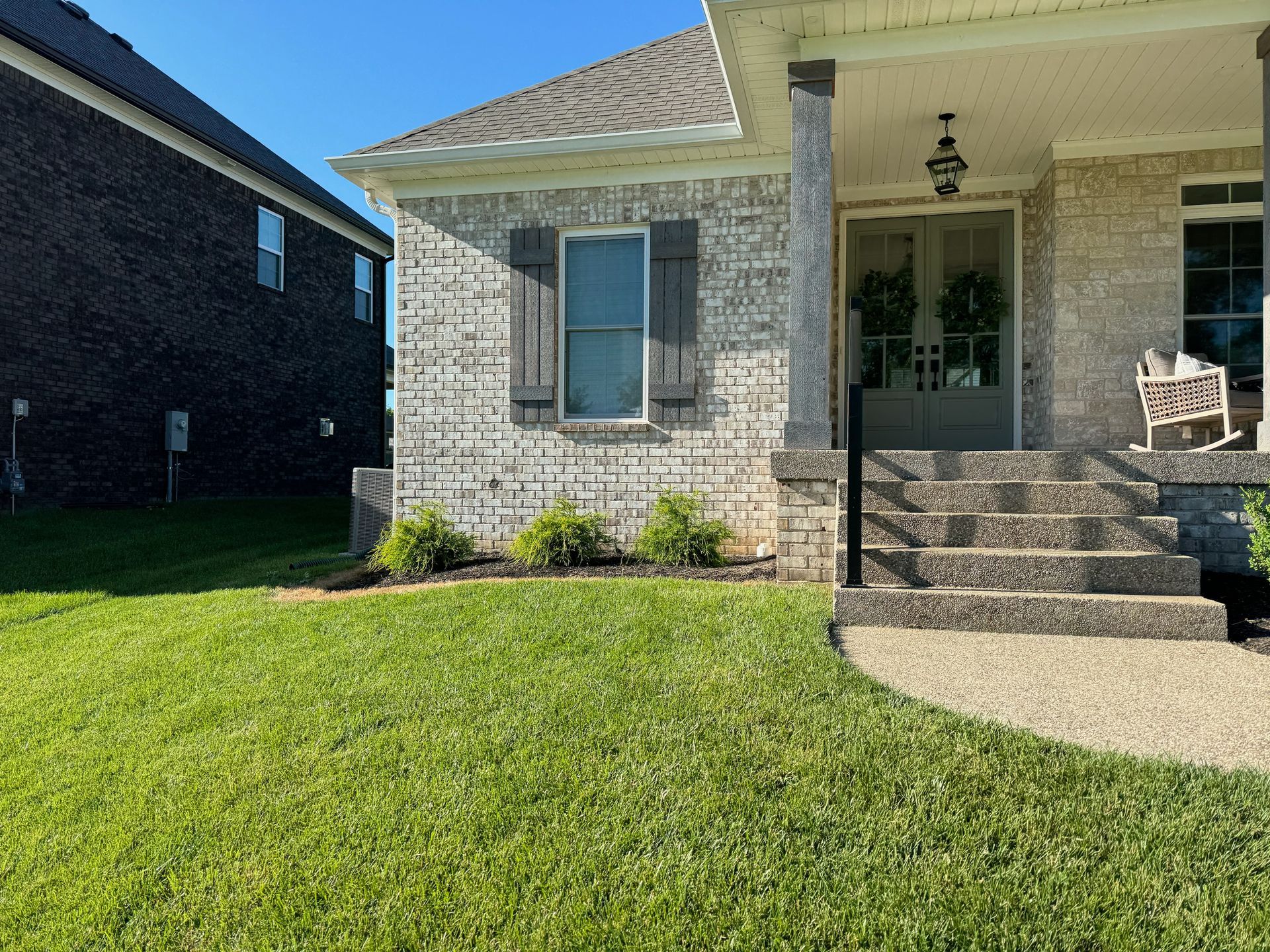 Exterior of a brick home with a manicured lawn. Gray shutters and a green front door are visible.