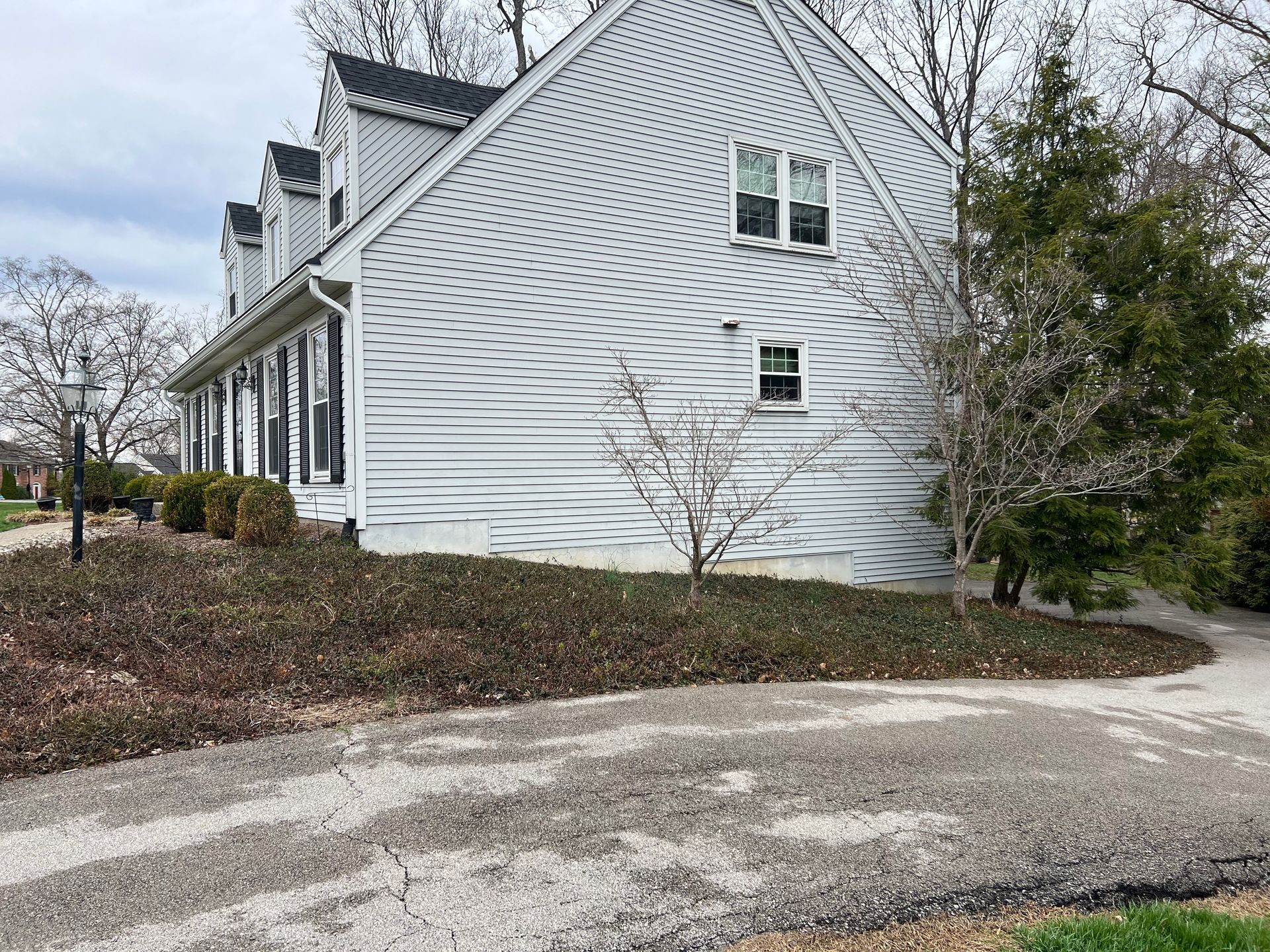 Side view of a two-story house with white siding, a gravel driveway, and a bed of brown and green plants.