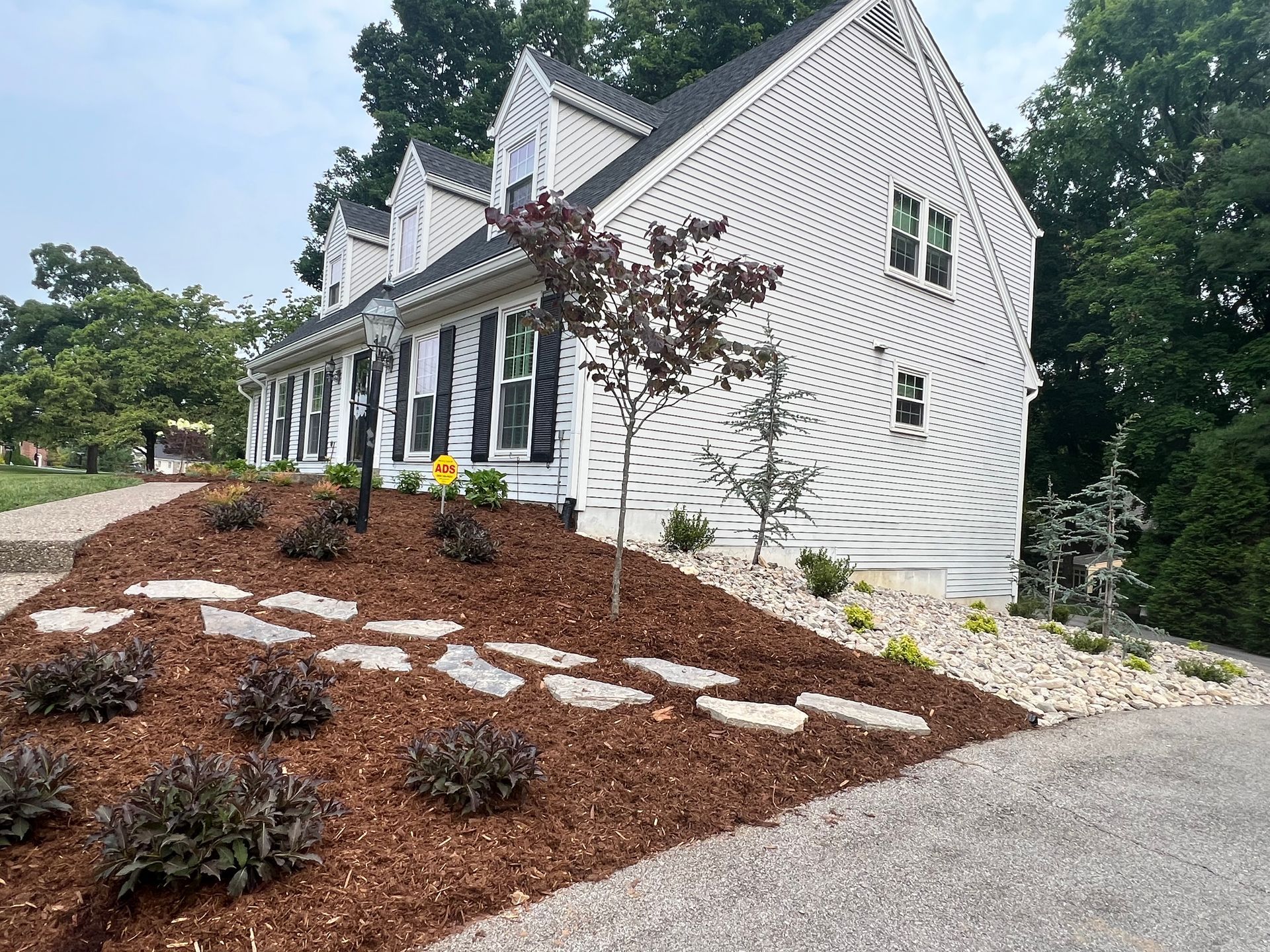 White house with black shutters and a landscaped front yard with a stone pathway and mulch.
