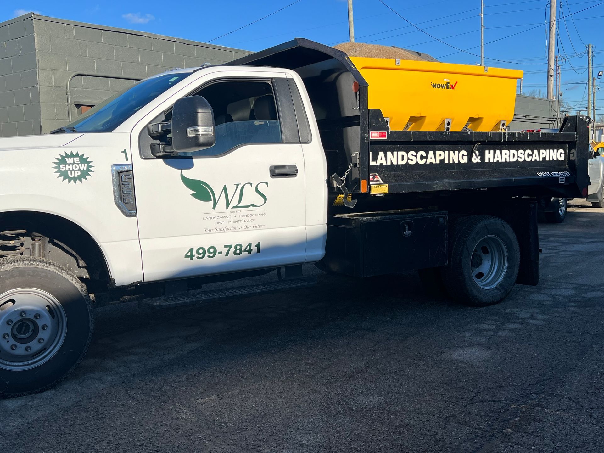 White landscaping dump truck with yellow equipment parked outdoors on a sunny day.